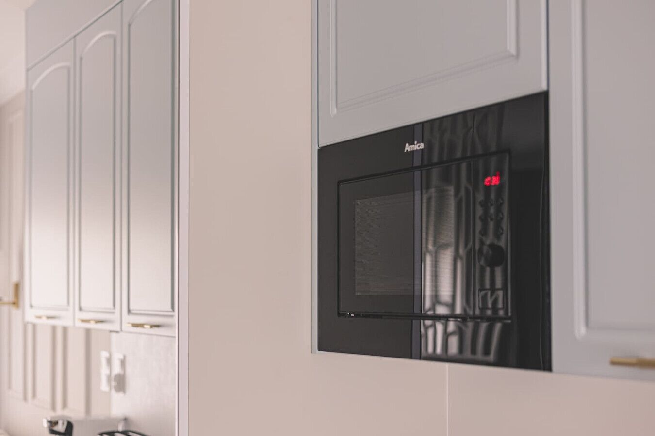 Une cuisine avec des meubles blancs et un four à micro-ondes noir de la marque « Amica ».