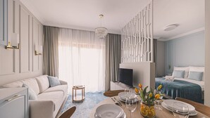 Ein modernes Hotelzimmer mit Essbereich, einer Sitzecke, einem Fernseher und einem Bett mit blauer Kopfteil.