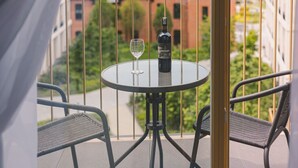 Ein Balkon mit rundem Tisch, zwei Korbstühlen, einer Flasche und einem Weinglas.