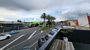 A street view with cars parked along the road, a green building with a sign, and palm trees. - Rooftop Apartments (Raglan)