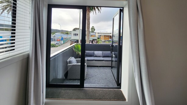 A balcony with a sliding glass door, a grey sofa, and a small table. - Rooftop Apartments (Raglan)