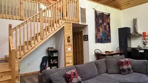A cozy living room with a gray sofa, wooden staircase, and a kitchen area.