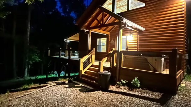 A wooden cabin with a porch, a staircase, and a gravel driveway.