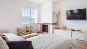 A bedroom with a large bed, a fireplace, a TV, and a window with a view.