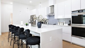 A modern kitchen with white cabinetry, a central island with bar stools, stainless steel appliances, and a herringbone-patterned backsplash. - Spacious 4-bedroom house Game Room & Spa in fantastic Dallas 11 (Dallas)