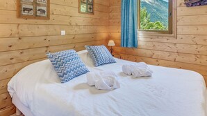 Habitación de cabaña de madera con cama, dos almohadas, ventana y vista a la montaña, además de una lámpara.