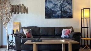 Un salón con sofá, mesa de centro, lámpara y un cuadro en la pared.