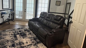 Ein Wohnzimmer mit einem Ledersofa, einem Glastisch, einem schwarz-weißen Teppich und einer Tür zu einer Treppe.