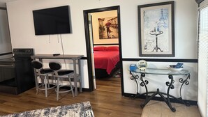 Ein kompakter Wohnbereich mit Küchenzeile, Essbereich, Wandfernseher und Bett mit roter Decke.