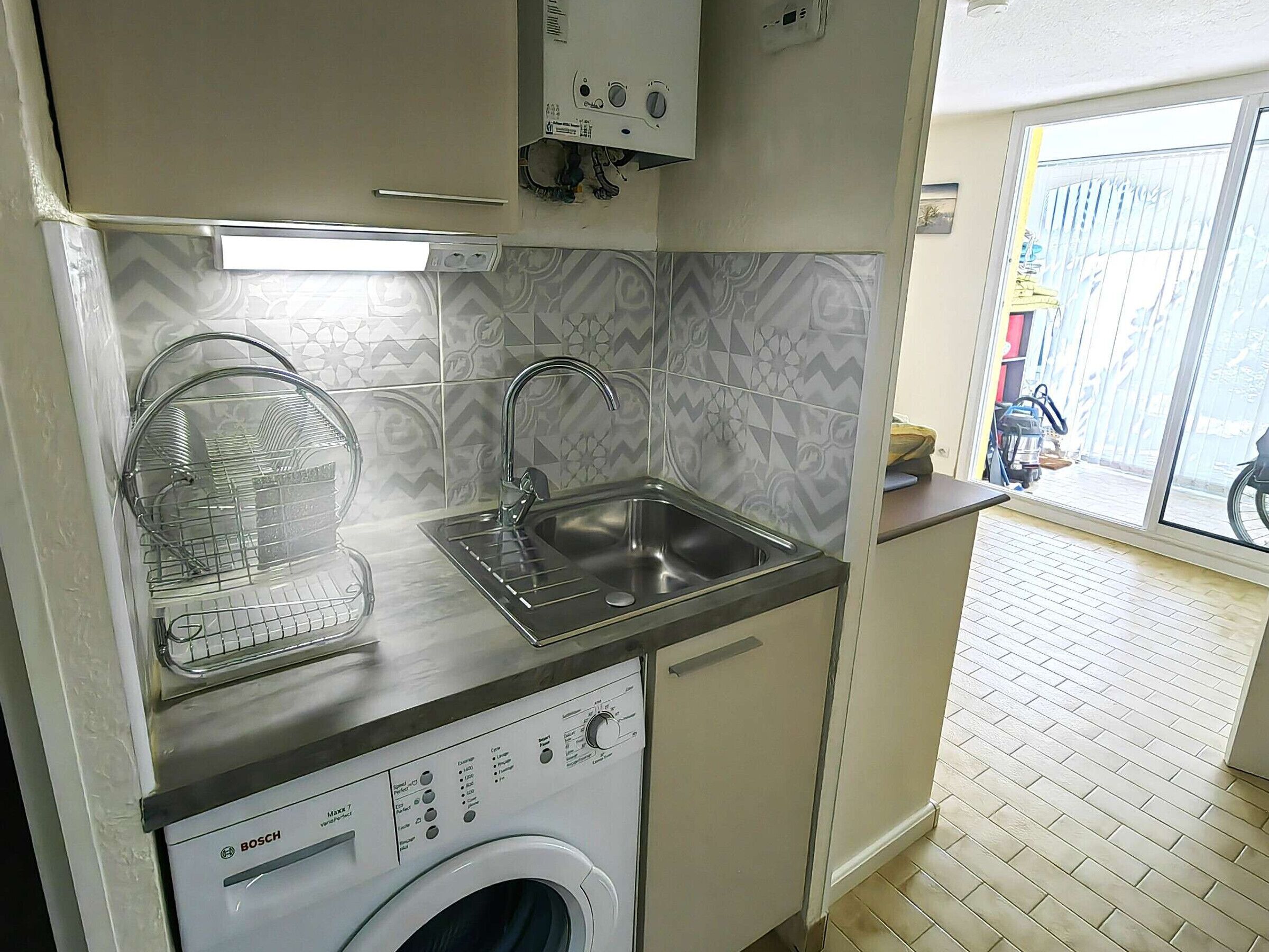 A compact kitchen with a Bosch washing machine, a sink, and a dish rack.