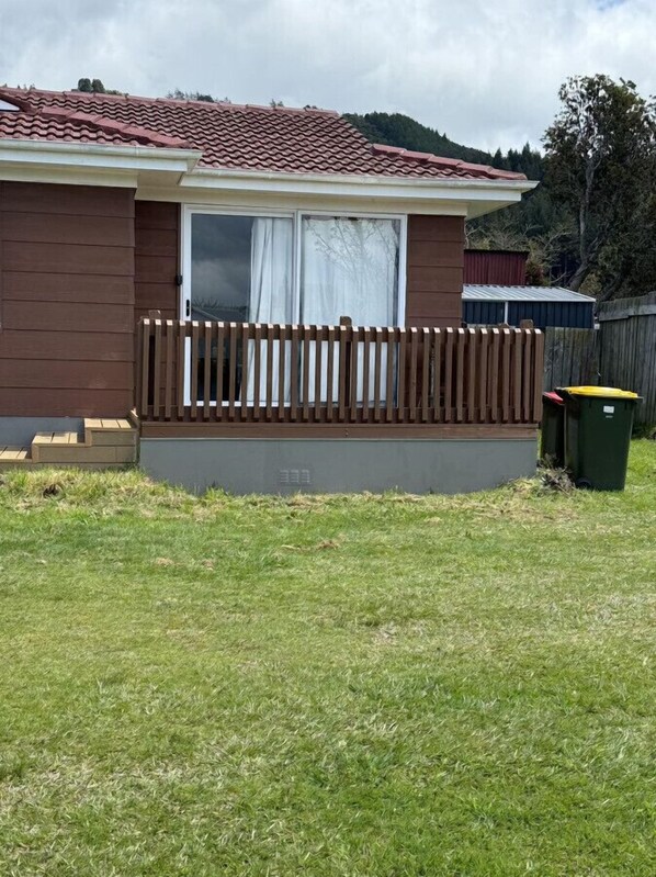 A single-story house with a red-tiled roof, a wooden deck, and a grassy yard. - 2 Double 1 Single 1 Sofa Beds Studio A (Rotorua)