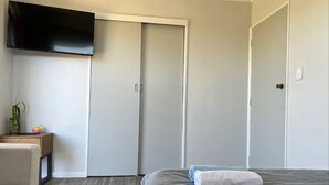A bedroom with a bed, a TV mounted on the wall, and a wardrobe. - 2 Double 1 Single 1 Sofa Beds Studio A (Rotorua)