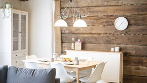 A modern dining area with a wooden wall, a clock, and a white cabinet. - Chasa Rustica – Modern 3-Room Apartment with Traditional Charm in Sent (Sent)