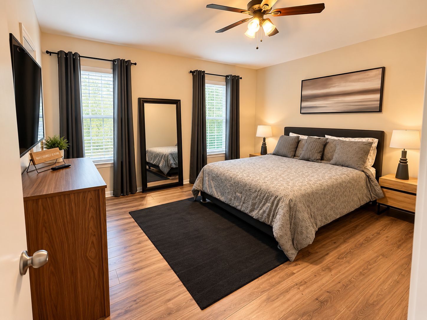 A bedroom with a bed, bedside lamps, a ceiling fan, and a large mirror.