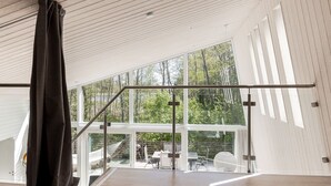 A spacious room with a high ceiling, large windows offering a view of a forest, and a modern staircase. - Lagunen Villa 3 by Interhome (Hölick)