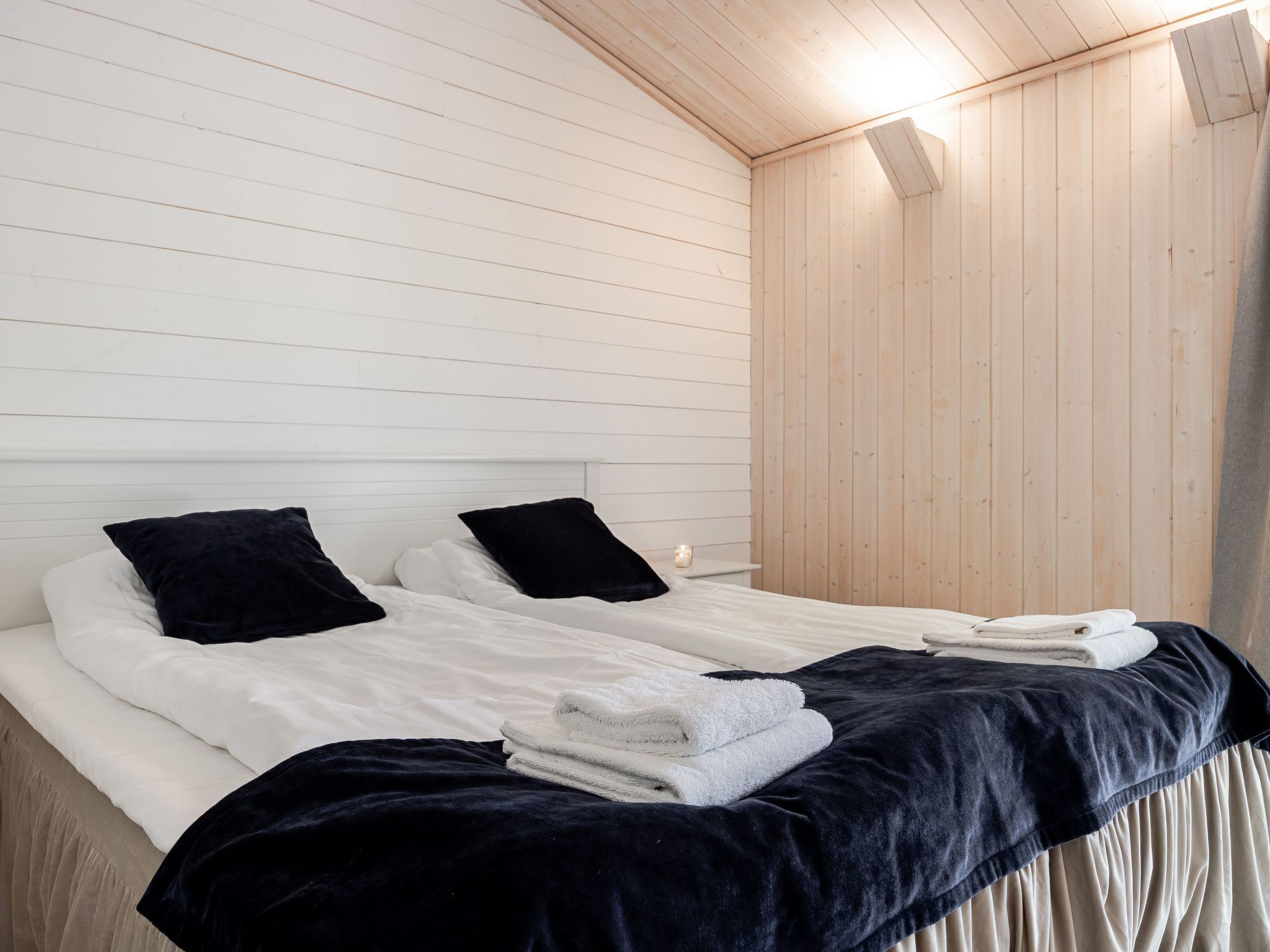 A double bed with white linens and black pillows, a dark blue blanket, and folded towels.