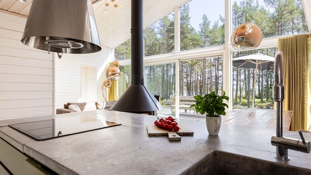 Een moderne keuken met een groot raam, een centraal geplaatst fornuis, en een zithoek met een bank en tafel.