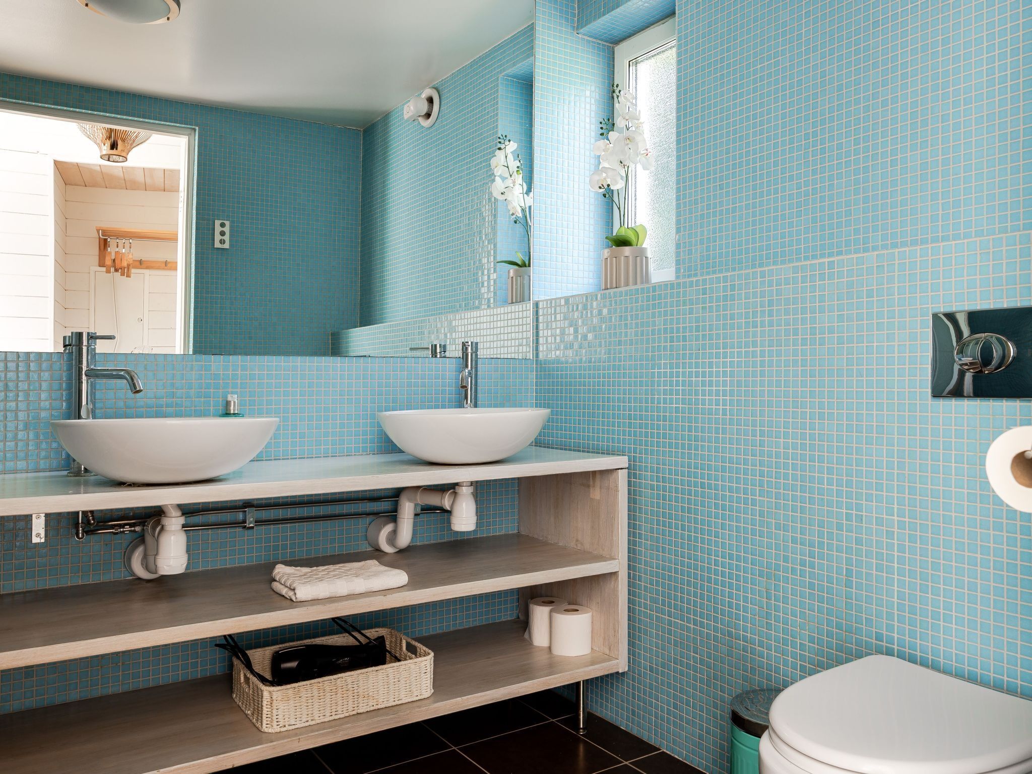 Een badkamer met twee wastafels, een spiegel, een toilet en een plank met handdoeken en toiletartikelen.