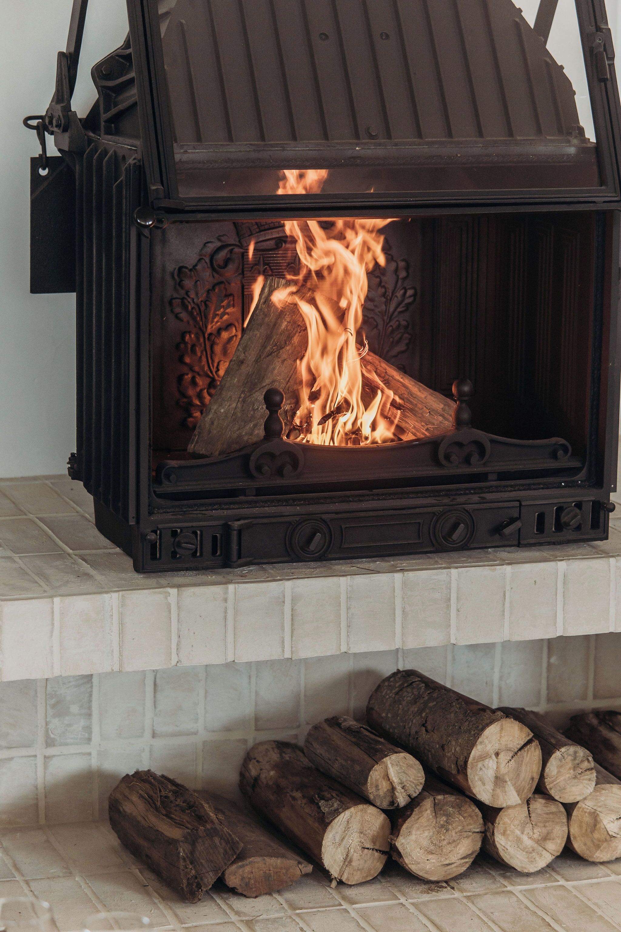 Una estufa de leña con fuego encendido, ubicada en un hogar de chimenea con azulejos.