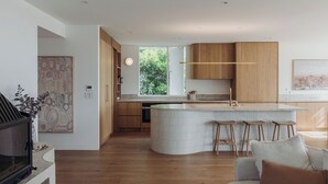 A modern kitchen with wooden cabinets, a curved island with stools, and a large window providing natural light.