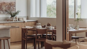 A cozy dining area with wooden furniture, a large window, and a view of greenery outside.
