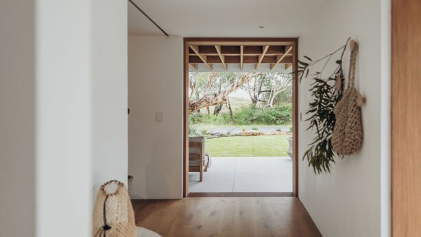 A hallway with a wooden floor leading to a glass door opening to a garden.