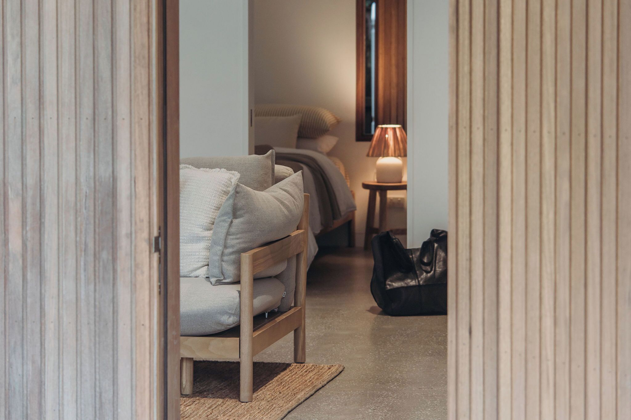 Ein enger Flur, der zu einem Schlafzimmer führt, mit einem Bett, einem Nachttisch mit Lampe und einer Tasche auf dem Boden.