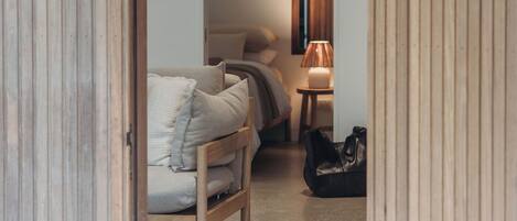 Ein enger Flur, der zu einem Schlafzimmer führt, mit einem Bett, einem Nachttisch mit Lampe und einer Tasche auf dem Boden.