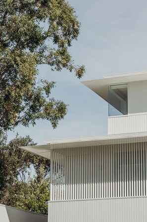 A modern building with a flat roof, a balcony with vertical siding, and a large window on the upper floor. - Osprey at Hawks Nest - Entire Property (Hawks Nest)