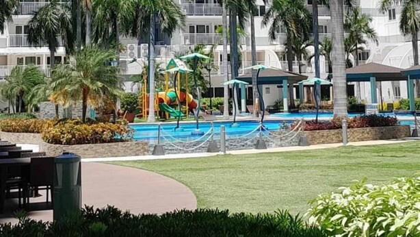 A high-rise hotel with multiple balconies, a swimming pool, and palm trees. - Cozy 1-bedroom condo in beautiful Pasay City with WiFi, AC (Pasay city)