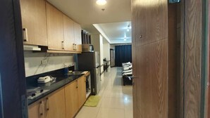 A narrow hallway with a kitchen on one side, featuring wooden cabinets, a black countertop, and a refrigerator. - Cozy 1-bedroom condo in beautiful Pasay City with WiFi, AC (Pasay city)