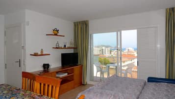A hotel room with a bed, a desk with a television, a chair, and a balcony with a view of the city.