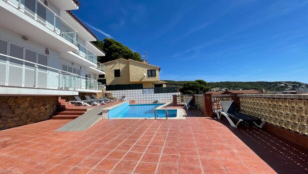 A rooftop pool area with a clear view of a hillside and a building in the background. - Apartment in Spain near Sandy Beach (Estartit)