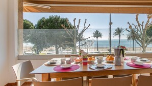 Un comedor con una mesa lista para cuatro personas, con vista a una playa con palmeras y el océano.