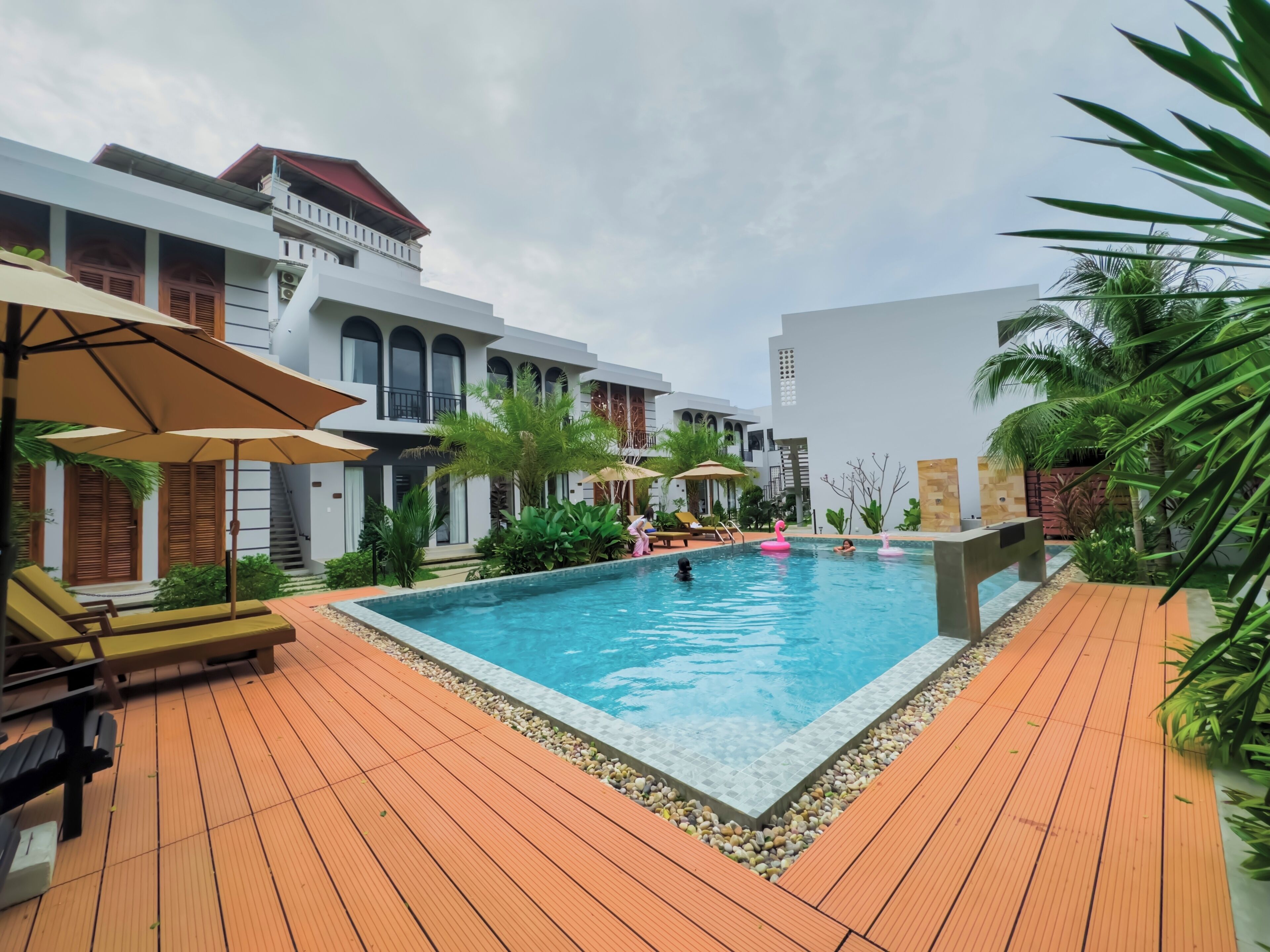 A swimming pool surrounded by wooden deck, with lounge chairs and umbrellas.
