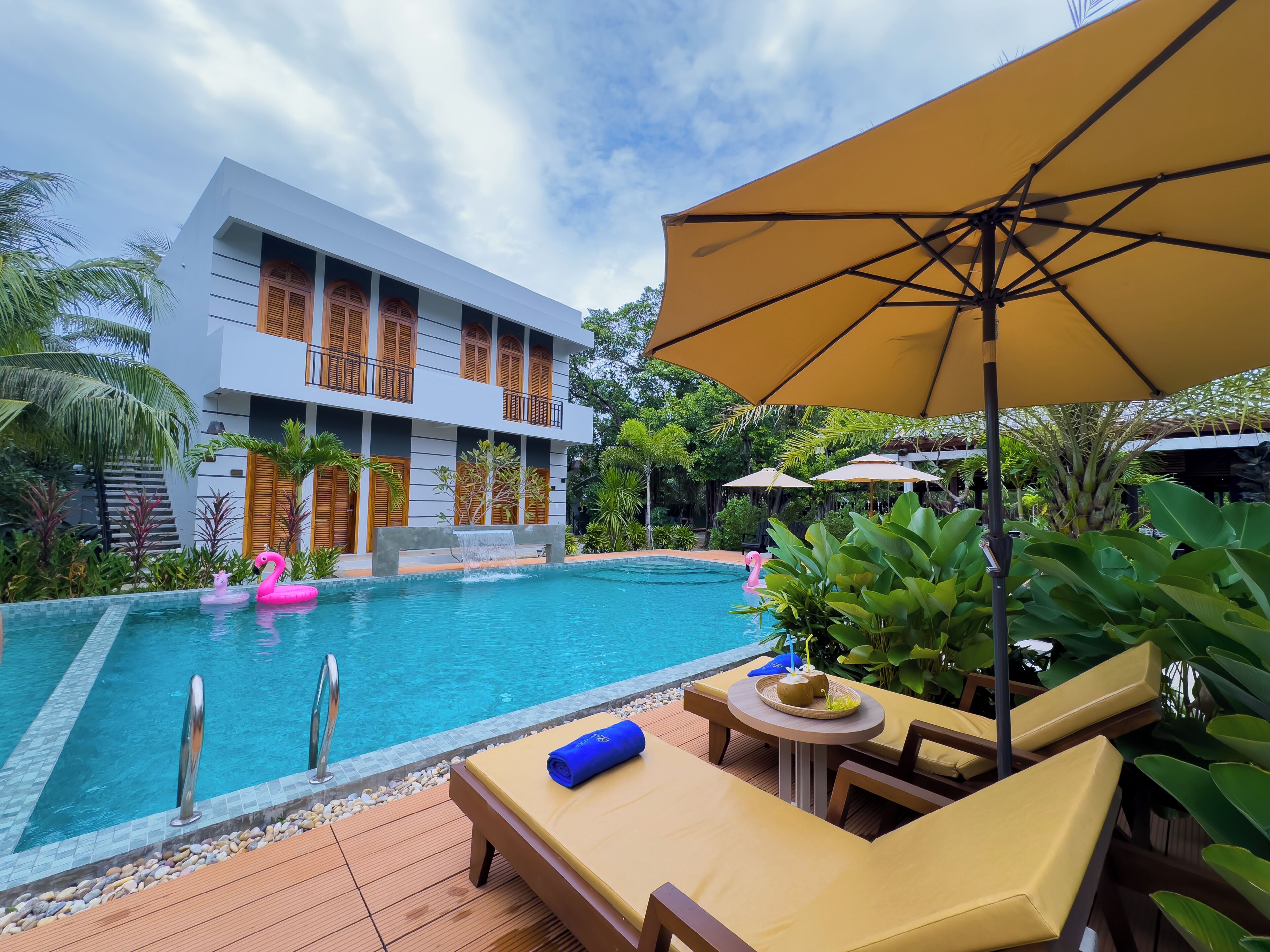 A pool area with lounge chairs and umbrellas, a modern building with balconies, and a clear blue sky.