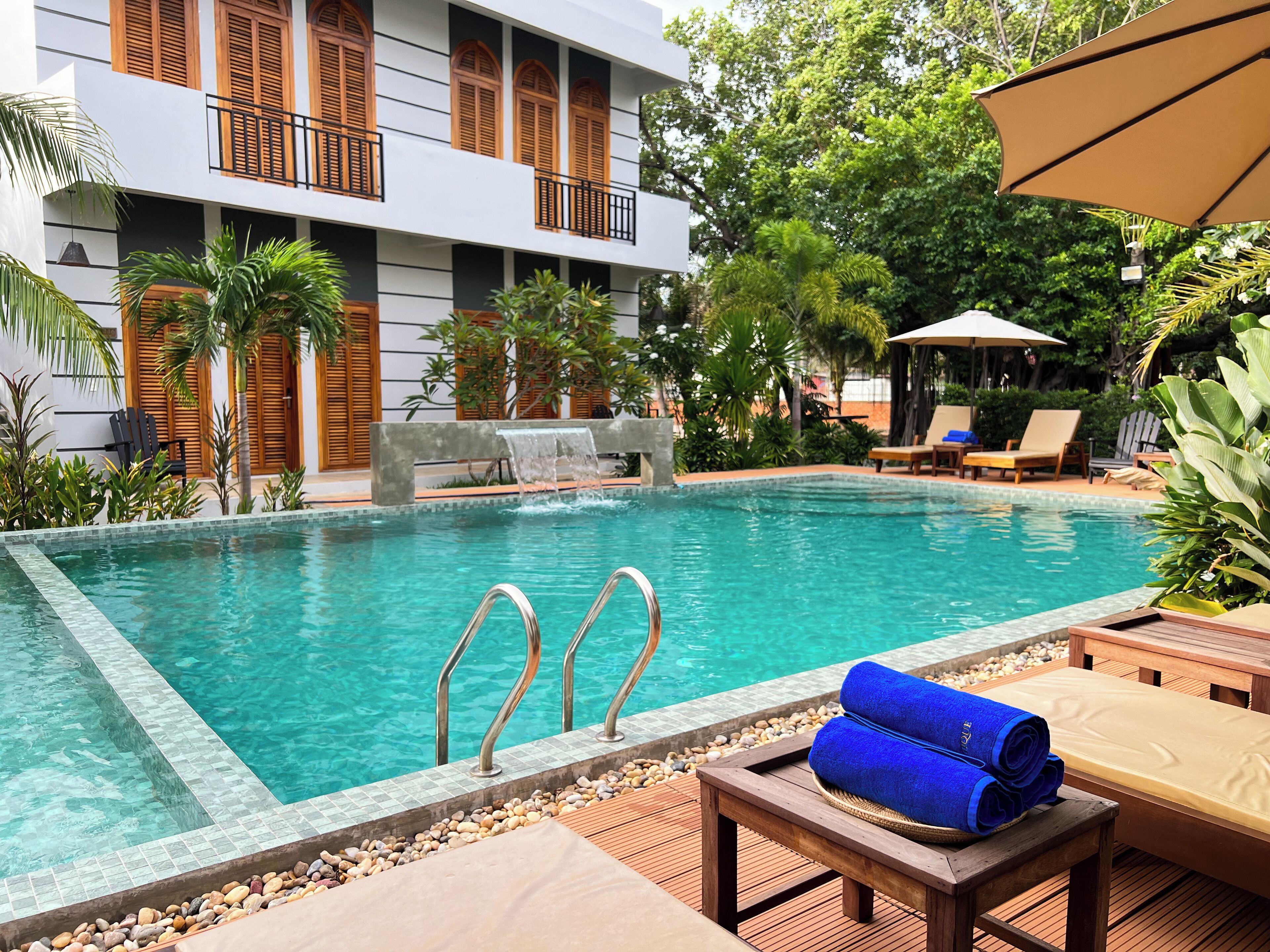 A pool area with a clear blue pool, wooden deck, lounge chairs, and a waterfall feature.