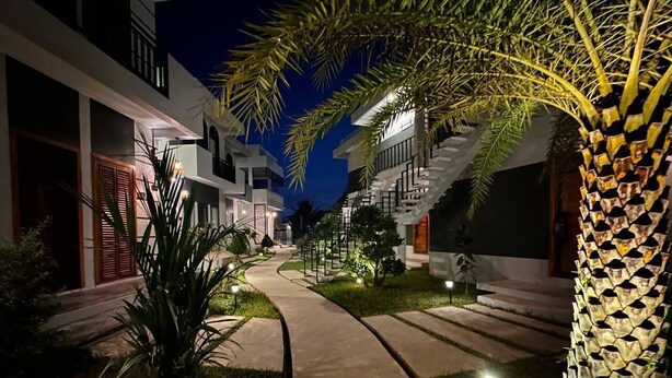 A nighttime view of a modern hotel with a central pathway, palm trees, and illuminated steps leading to the entrance. - The R&B Boutique (Kampot)