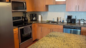 A modern kitchen with granite countertops, stainless steel appliances, wooden cabinets, and a hanging pendant light. - FIFA World Cup - SuiteHearts Buckhead (Atlanta)