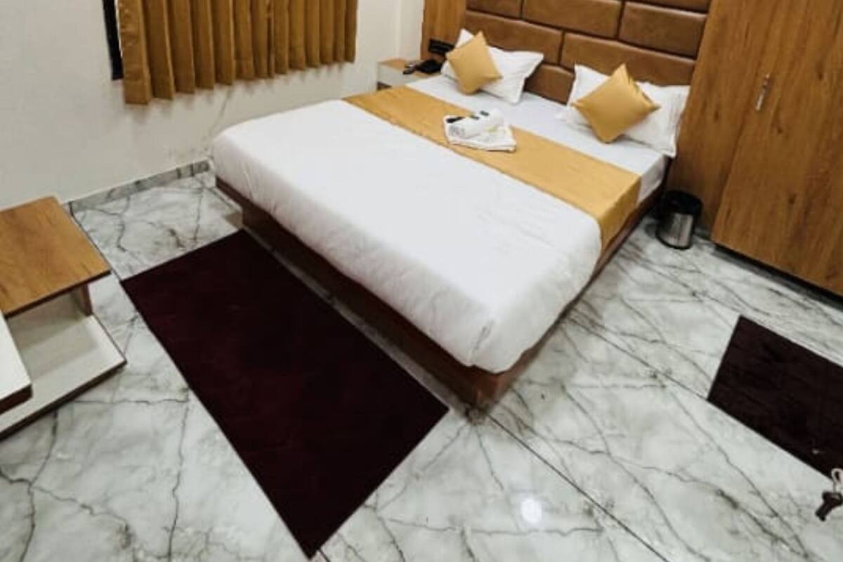 A hotel room with a bed, a wooden headboard, a ceiling fan, a window with blinds, a marble floor, and a bedside table.