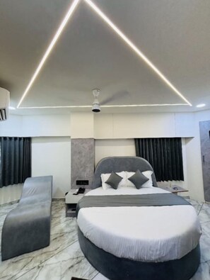 A modern bedroom with a large bed, a bedside table, a nightstand, a ceiling fan, and a headboard. - The Azone Hotel (Ahmedabad)