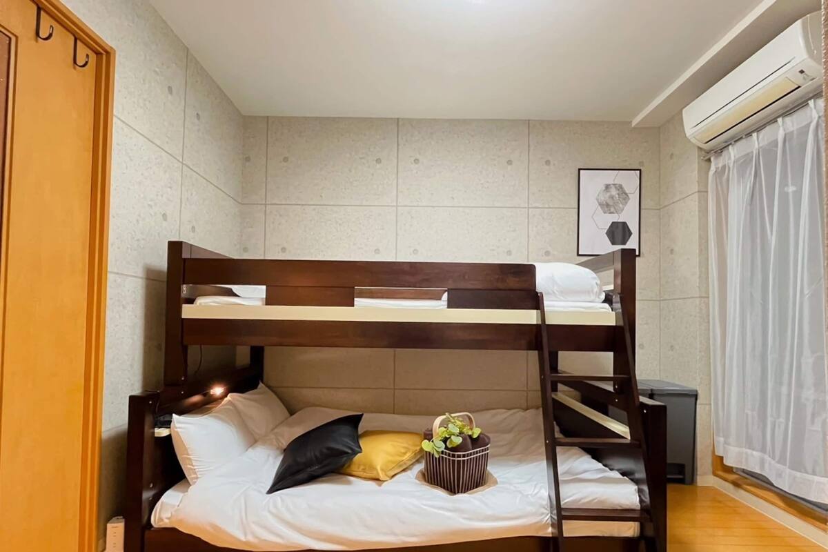 Una cama litera con estructura de madera, una mesita de noche, una planta pequeña y un cuadro en la pared.