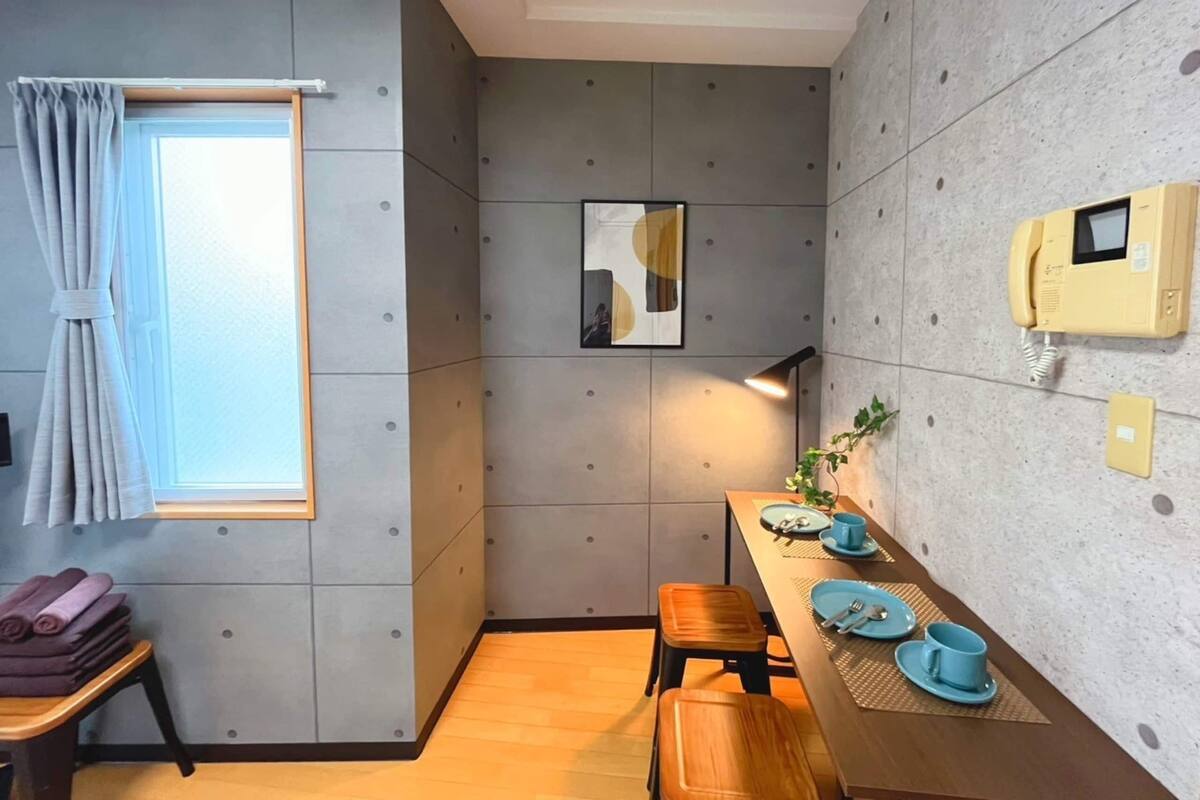 Una cocina compacta con comedor, una ventana con cortinas, un teléfono de pared y una pequeña mesa con platos y tazas azules.
