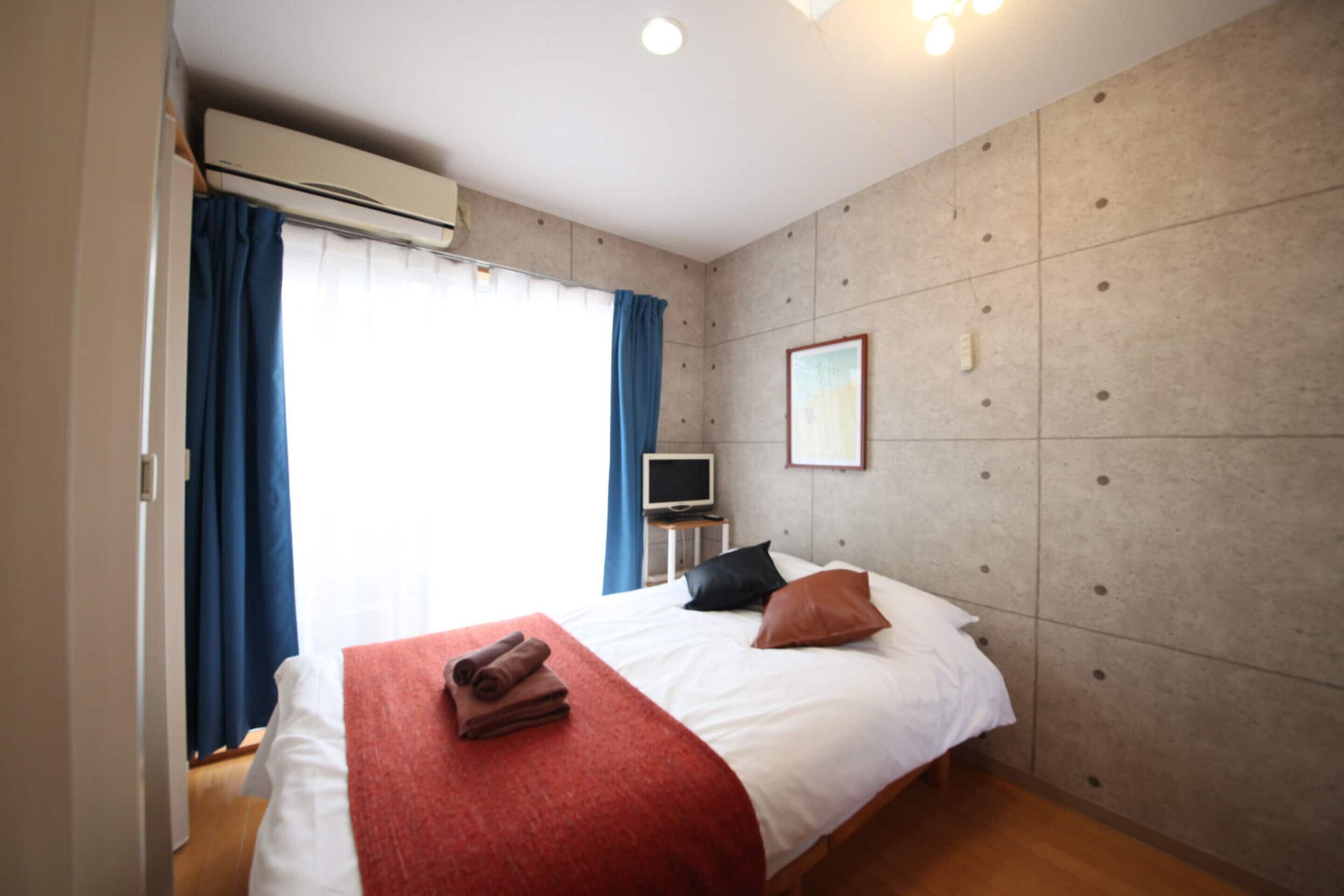 Una habitación de hotel con cama, televisión, aire acondicionado y una ventana con cortinas.