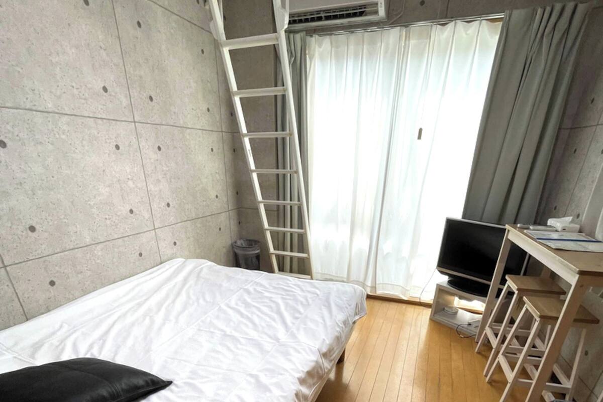 Una habitación con cama, escritorio, televisor, escalera y unidad de aire acondicionado.