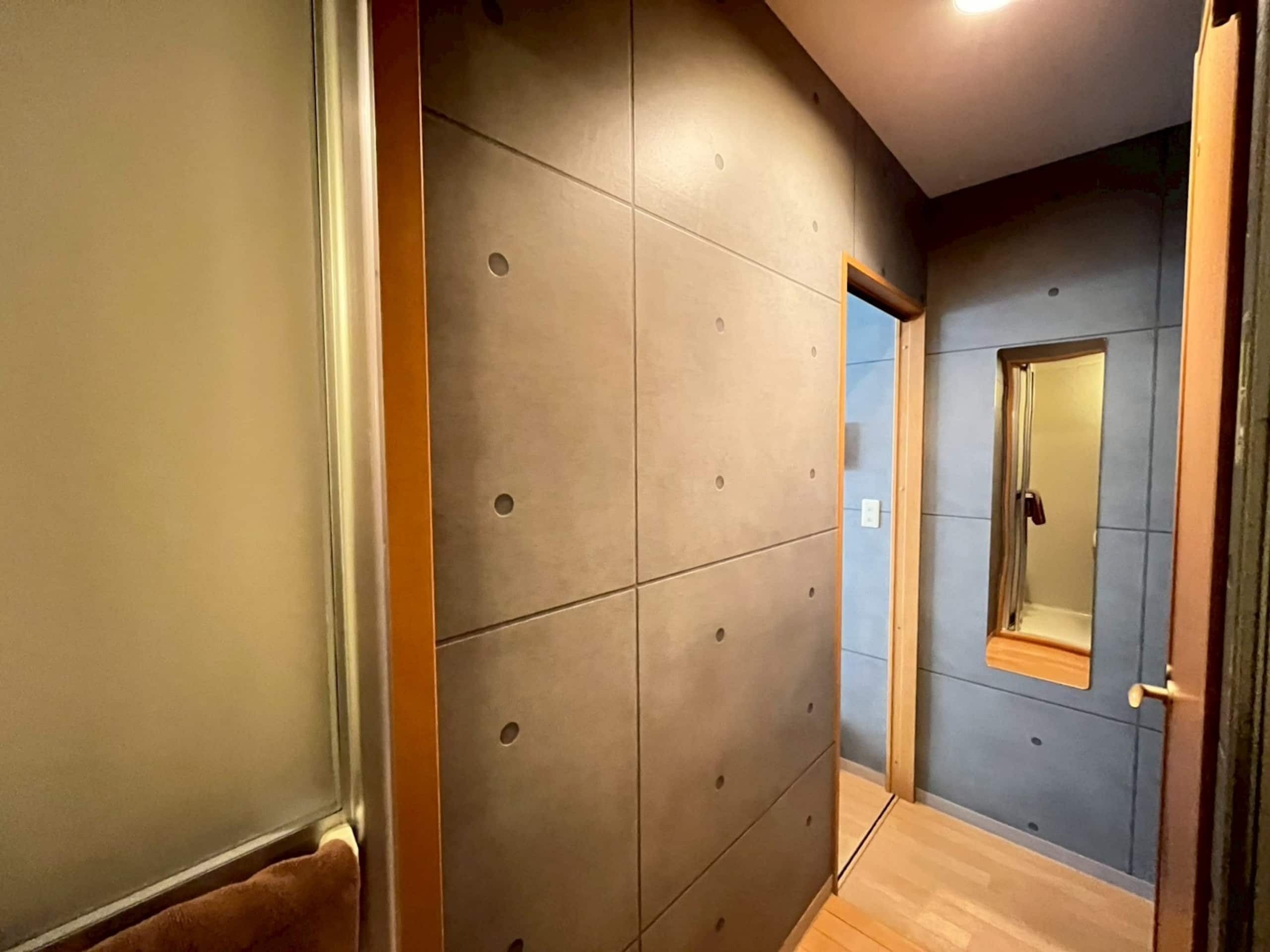 Un corridoio con pavimento in legno, una porta con specchio e una parete a griglia.