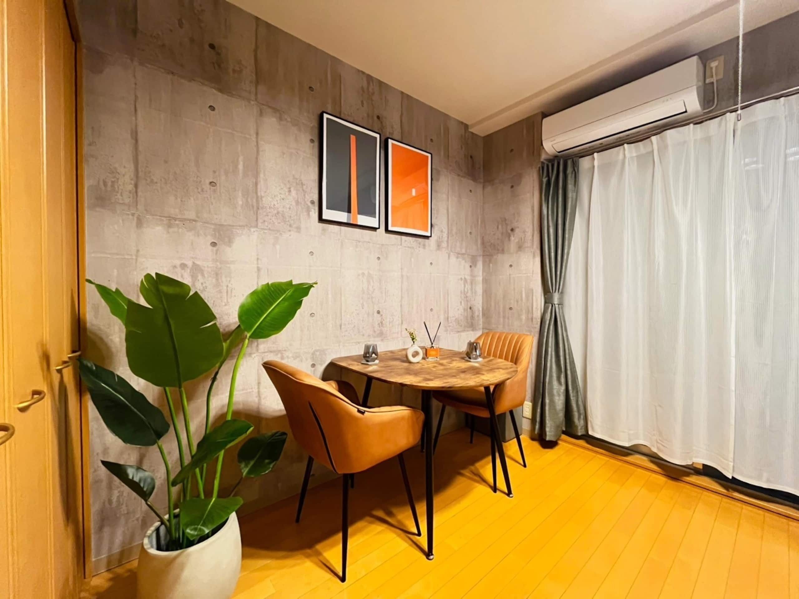 A dining area with a wooden table, chairs, a potted plant, and artwork on the wall.
