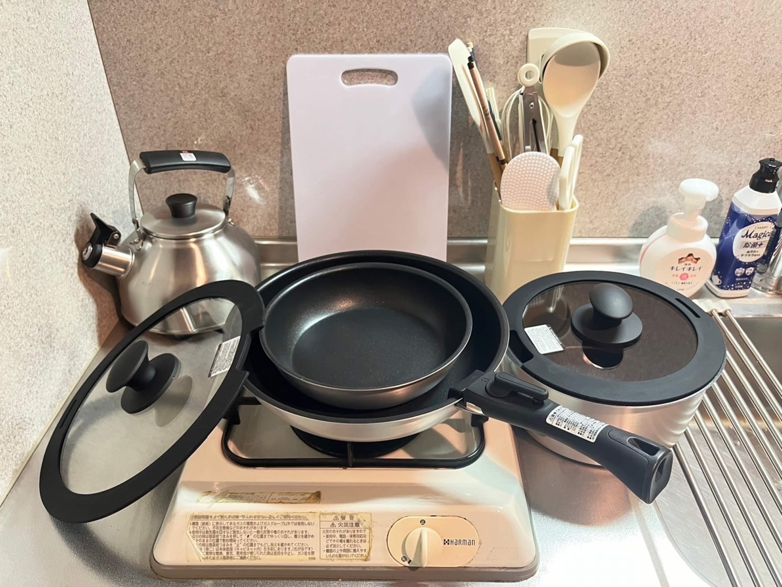 A kitchen with a gas stove, a frying pan, a pot, a kettle, and various utensils.