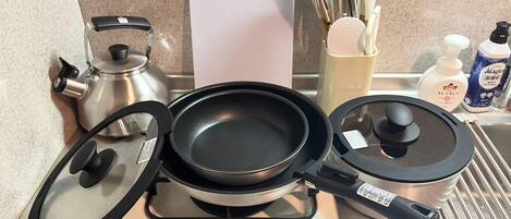 A kitchen with a gas stove, a frying pan, a pot, a kettle, and various utensils.