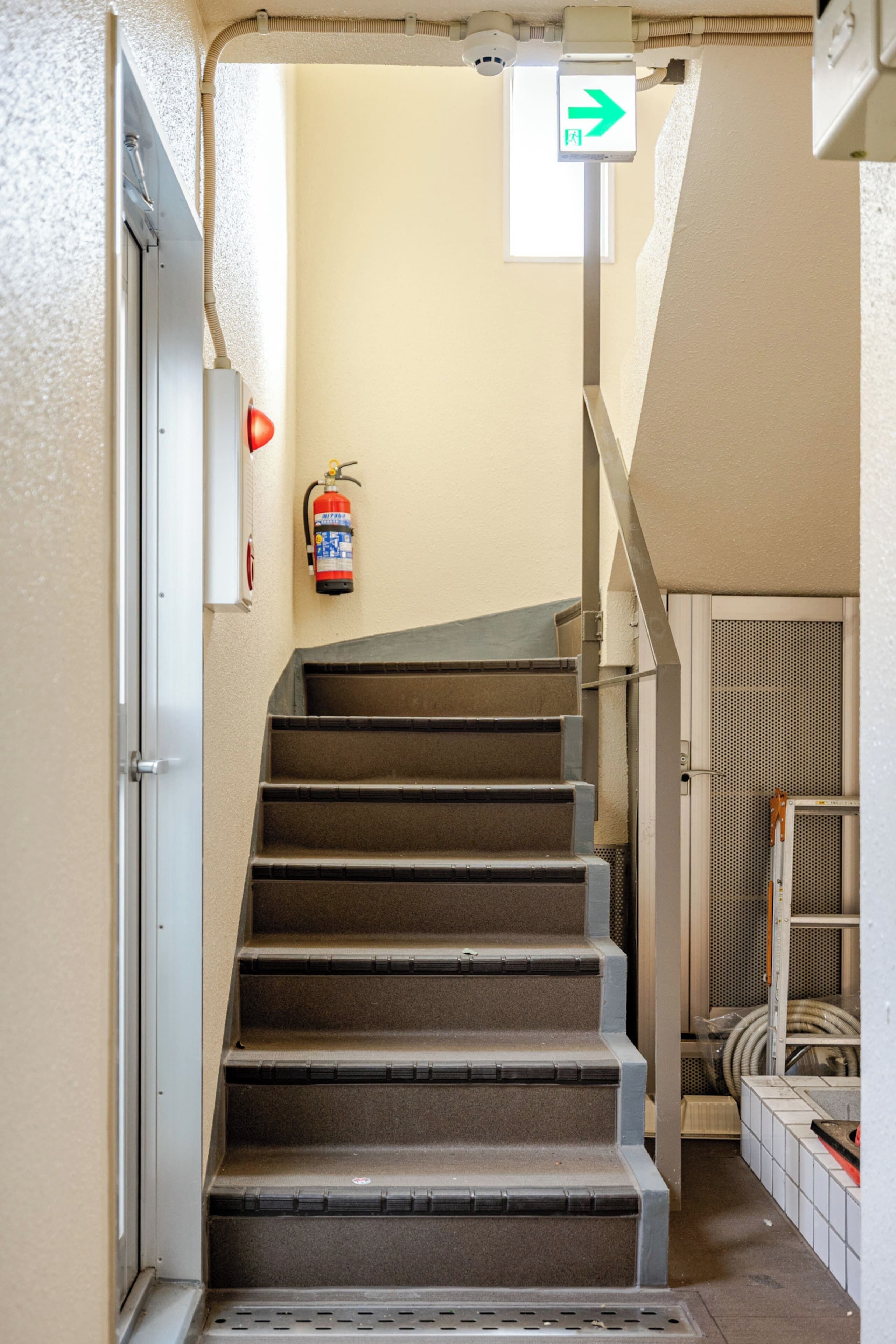 A staircase with a fire extinguisher mounted on the wall, a directional sign, and a metal railing.